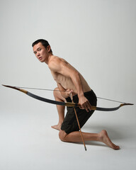 Full length portrait of fit  asian male model,  Holding hunting bow and arrow archery weapon,...