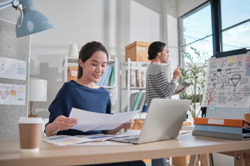 Two young Asian startup company partners concentrate and think in a casual small business office, working jobs with tablet and laptop, as online freelance E-commerce entrepreneurs and coworker team.