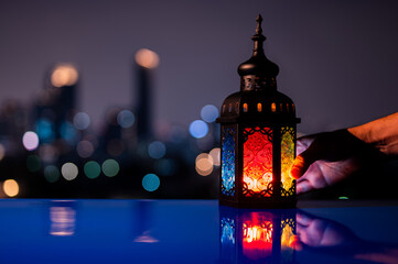Lantern holding by hand on table with night sky and city bokeh light background for the Muslim feast of the holy month of Ramadan Kareem.