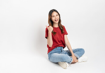 Happy smiling young woman sitting and shows hand pointing to the top, isolated on white background.