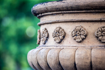 A decorated terracotta garden urn is weathered by the elements and set against a green background