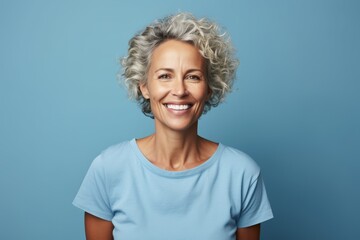 Cheerful mature woman looking at camera and smiling while standing against blue background