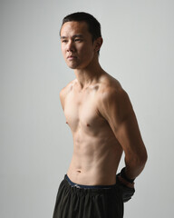 Close up portrait of fit  asian male model, shirtless with muscles. Wearing gym shorthand boxing gloves, gestural punching pose. Isolated on a white studio background.