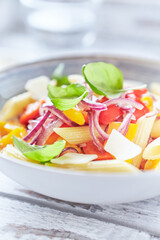 Penne pasta with yellow and red pepper, hard cheese and fresh basil. Bright background. Close up.	