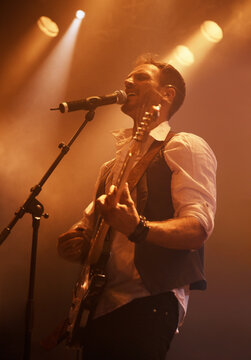 Concert, singer and guitar with man on stage for music, performance and rock show. Event, spotlight and energy with male musician playing instrument at festival club for rave, disco and celebration