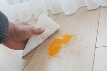 A man's hand washing the floor with a tissue cleaning egg spill 