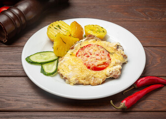 Pork baked with cheese and boiled potatoes. On a wooden background.