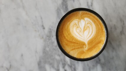 Top view of a cup of cappuccino on a marble table with negative space to the left of the object
