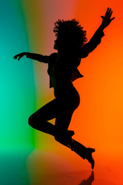 Silhouette of a woman dancer with afro leaping against a gradient background in green to orange