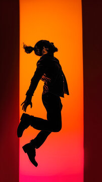 Excited man with ponytail jumping free and energetic against a vibrant orange studio background
