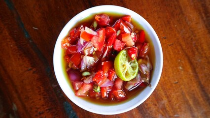Sambal matah served on white bowl, traditional Balinese chili sauce made from raw ingredients . The ingredients for sambal matah are: shallots, chilies, shrimp paste, salt, lemongrass, and lemon