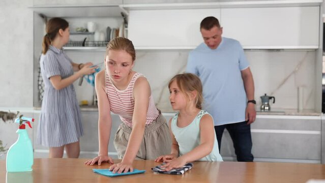 Teenage girl actively participating in household chores by assisting family in cleaning apartment, wiping kitchen table. Concept of beneficial practice of involving teenagers in household chores