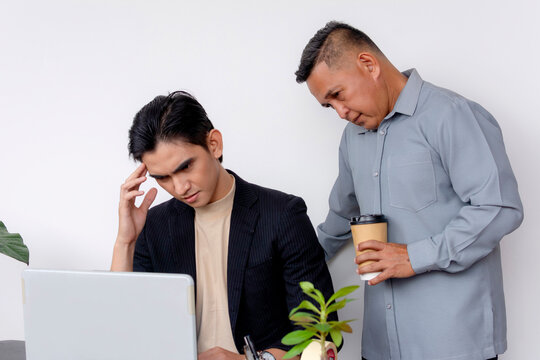 A stern and overbearing boss puts pressure on a visibly stressed man to complete deadlines on his work. A tough and taxing work environment. Negative effects of micromanagement.