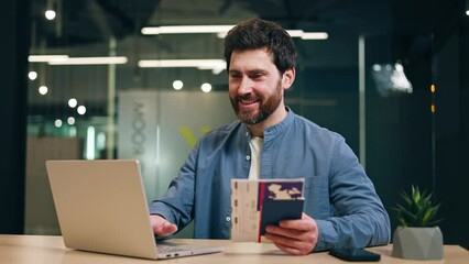 Satisfied entrepreneur using computer while resting hand with cruise admission ticket in passport on desktop with succulent. Happy man checking living conditions in cabin on ship on company website.