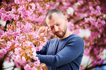 Man allergic suffering from seasonal allergy at spring in blossoming garden at springtime. Bearded...