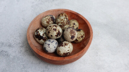 Raw quail egg in wooden bowl isolated on grey background