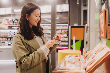 Beautiful woman testing and buying cosmetics in a beauty store. Young girl trying lipstick on hand...