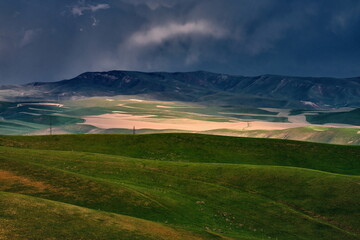 An epic landscape of spring hills against an approaching storm.