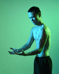 Close up portrait of fit asian male model, shirtless with muscles.  gestural ti chi inspired posing with arms reaching out  Isolated on a moody dark green studio background with silhouette.