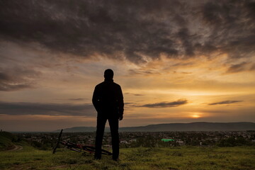 A person standing with their back to the viewer against the backdrop of a beautiful sunset, with a...