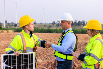 Engineer team standing shake hands in the meeting planing project install solar panel in the wind turbines farm.