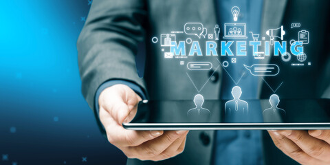 Close up of businessman hands holding tablet with creative marketing hologram with various icons on...