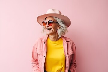 Portrait of a happy senior woman in hat and sunglasses over pink background