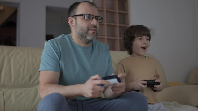 Father and Son Expressing Emotions While Enjoying Relaxing Together, Playing Video Games in Front of TV. Family Time Hobby. Family Having Fun Together at Home in Living Room Playing Video Games.