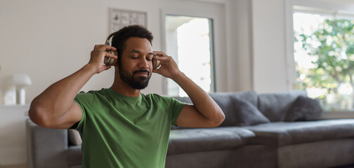 Young man with closed eyes, listening meditating music at home. Morning or evening workout routine,...