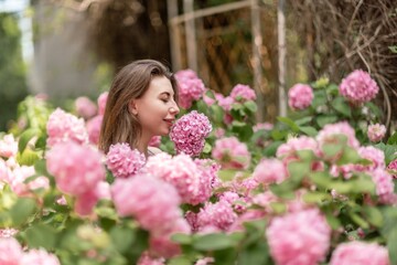 Hydrangeas Happy woman in pink dress amid hydrangeas. Large pink hydrangea caps surround woman. Sunny outdoor setting. Showcasing happy woman amid hydrangea bloom.