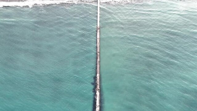 エメラルドグリーンの浅い海に浮かぶ、浜辺から伸びる桟橋を真上から