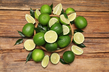 Fresh limes and green leaves on wooden table, flat lay