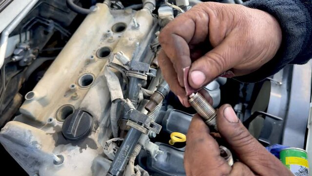 Cleaning a car engine spark plug with sandpaper in car garage.