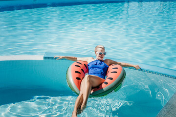 Happy woman in a swimsuit and sunglasses floating on an inflatable ring in the form of a watermelon, in the pool during summer holidays and vacations. Summer concept.