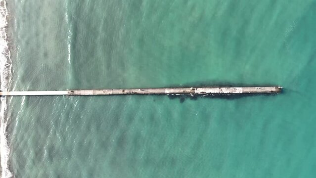 エメラルドグリーンの浅い海に浮かぶ、浜辺から伸びる桟橋を真上から