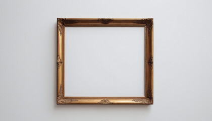 A classic, empty gold picture frame with intricate designs hangs against a white wall, exuding elegance and timeless sophistication.