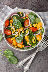 Organic low calorie salad of fresh spinach, corn, cherry tomatoes and red onion with olive oil dressing close up in a bowl on the table. Vertical top view from above