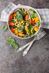 Summer salad of baby spinach, corn, cherry tomatoes and onions dressed with olive oil close-up in a bowl on the table. Vertical top view from above