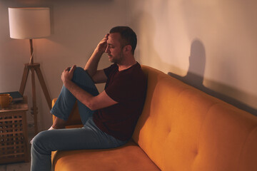 Man with headache and knee pain sitting on a sofa at home.