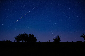 Milky way stars, shooting stars and countryside silhouettes photographed with wide angle lens.