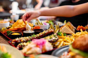 Woman dipping onion ring into bowl with sauce on table
