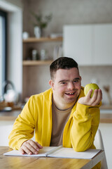 Portrait of young man with Down syndrome holding apple, sitting at table.