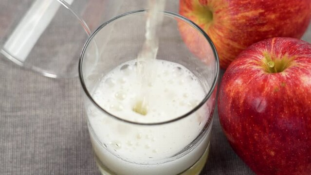 Pouring of Asturian Spanish apple cider into a drinking glass on table with red apples close up
