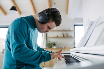 Young man with down syndrome playing on piano, listening his music via headphones.