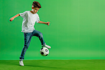Little boy playing with a soccer ball on green background.