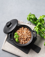 Buckwheat porridge in a black pan on a napkin on a light background with fresh herbs.