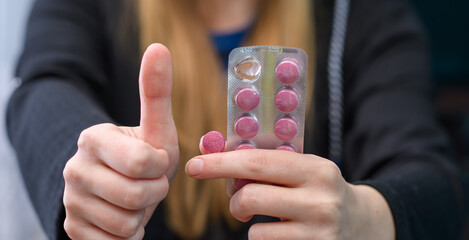 Kobieta trzyma w dłoni różowe tabletki i trzyma kciuk podniesiony w górę 