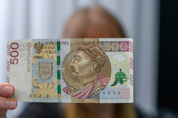 Kobieta trzyma w dłoni polski banknot 500zł, sprawdza czy nie jest fałszywy 