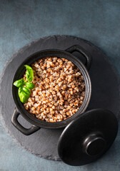 Buckwheat porridge with fresh herbs in a black pan on a board on a dark  background.
