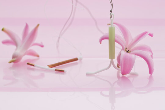 Close-up of intrauterine device leaning on pink hyacinthus blossom and intrauterine device with copper on light pink background